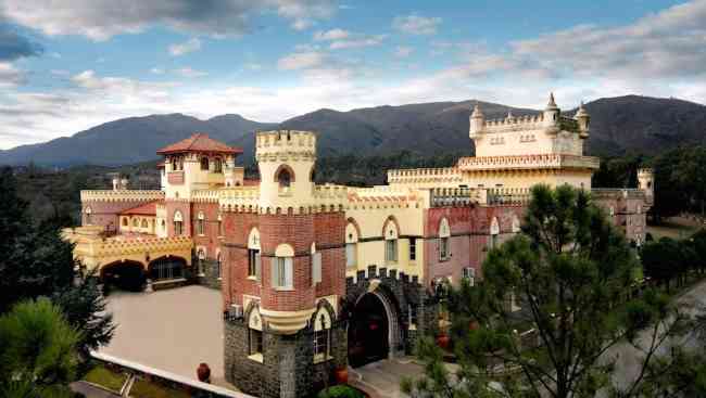 Vista desde la esquina de la fachada de un castillo con montañas de fondo.
